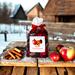 Apple Cinnamon Potpourri sitting on a wooden table next to apples and cinnamon sticks. There is an old farm and snow in the background.
